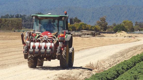 [image] Tractor on dirt road with trees and hills in the background