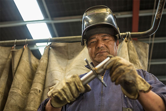 [Image] Manufacturing worker inspects machinery. 