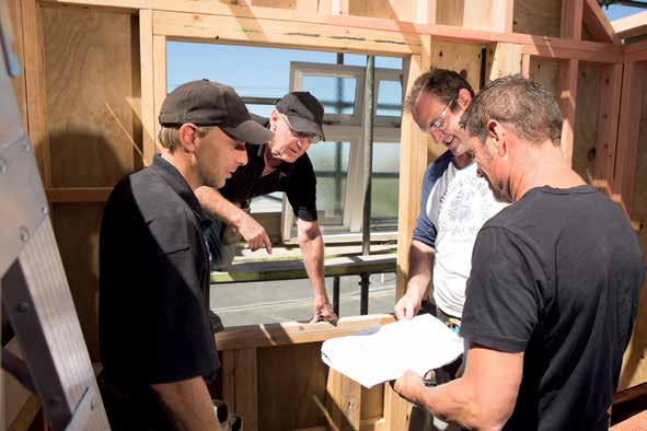 [image] four tradesmen standing in a building site looking at building plans