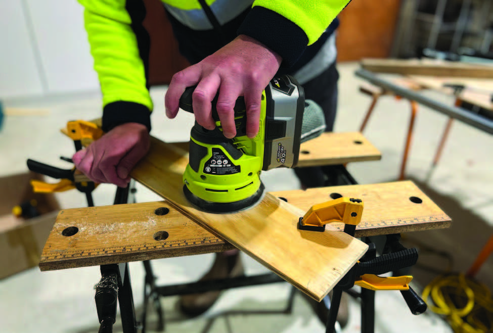 [image] photo of a person using an electric sander on a piece of wood clamped to a work bench