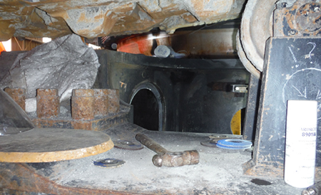 [image] View beneath excavator showing steel box section with inspection window and a hammer next to it