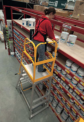 [image] To reach stock on high shelves, a worker uses a step platform with barriers on all sides